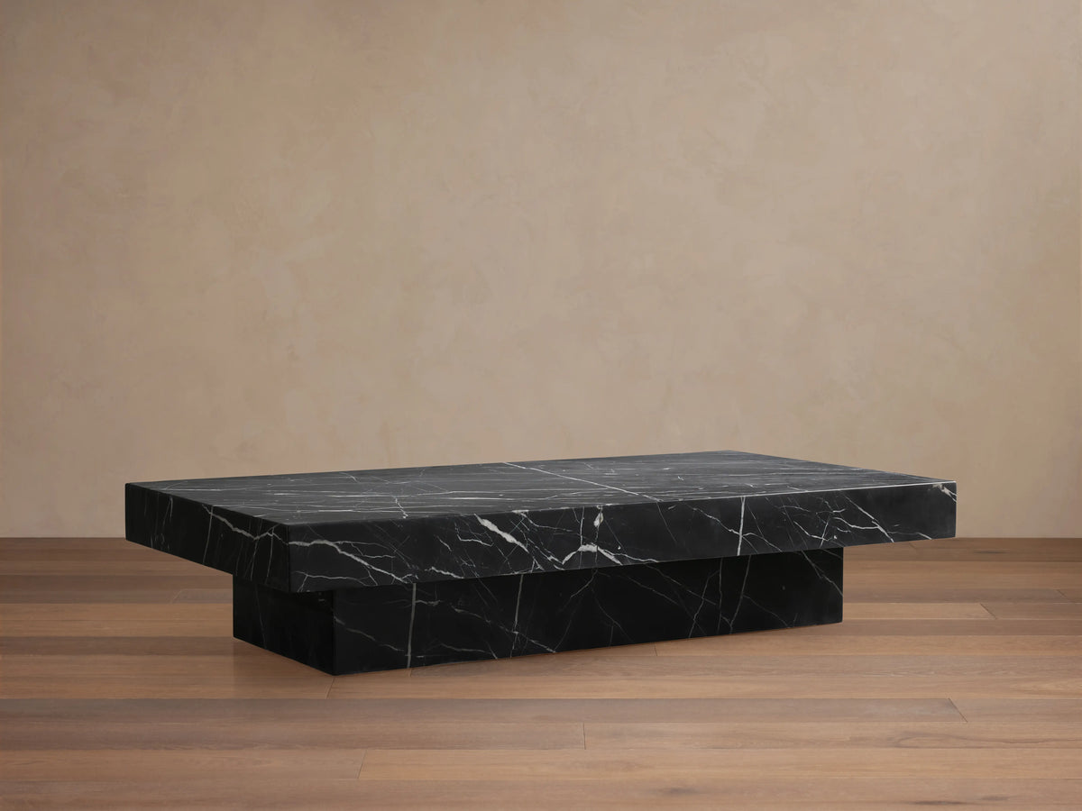 Cinzia Stone Coffee Table: low-profile, rectangular black marble with prominent white veining, plinth base, on a wooden floor.