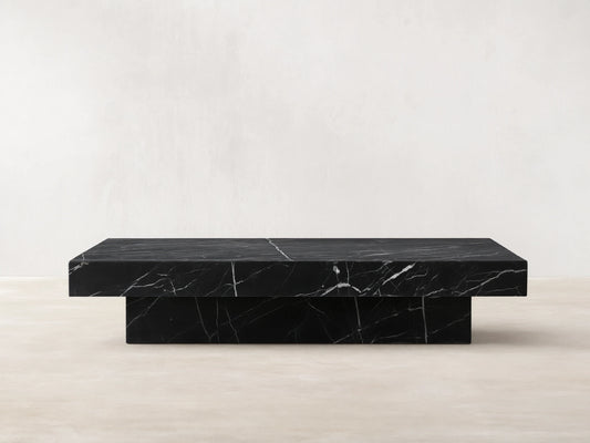 Cinzia Stone Coffee Table: low-profile, rectangular black marble with prominent white veining, plinth base, on a wooden floor.