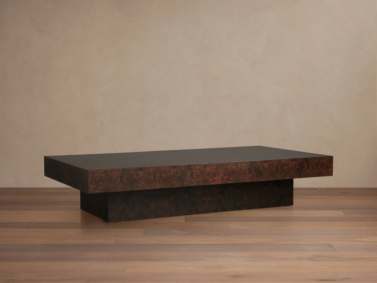 Cinzia Burl Coffee Table in walnut burl wood veneer with a low-profile, rectangular design on a plinth-style base, displayed on wood flooring.
