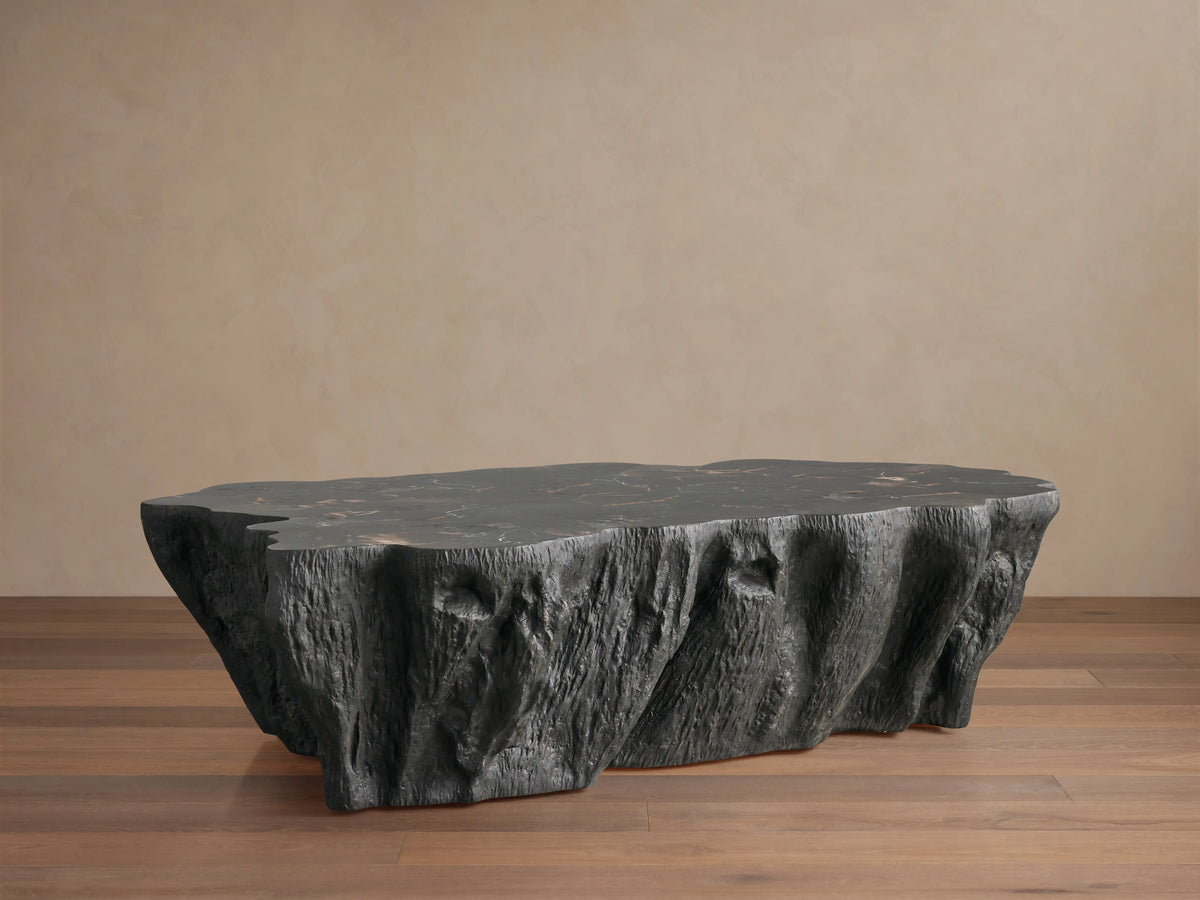 Clayhill Coffee Table with a dark petrified wood surface. The table has an irregular, sculptural form with textured sides, on a wooden floor.