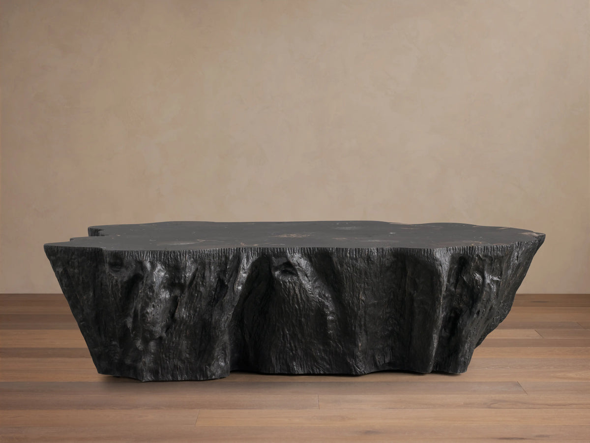 Clayhill Coffee Table with a polished, uneven petrified wood surface showcasing dark and light natural patterns, standing out against a beige background.