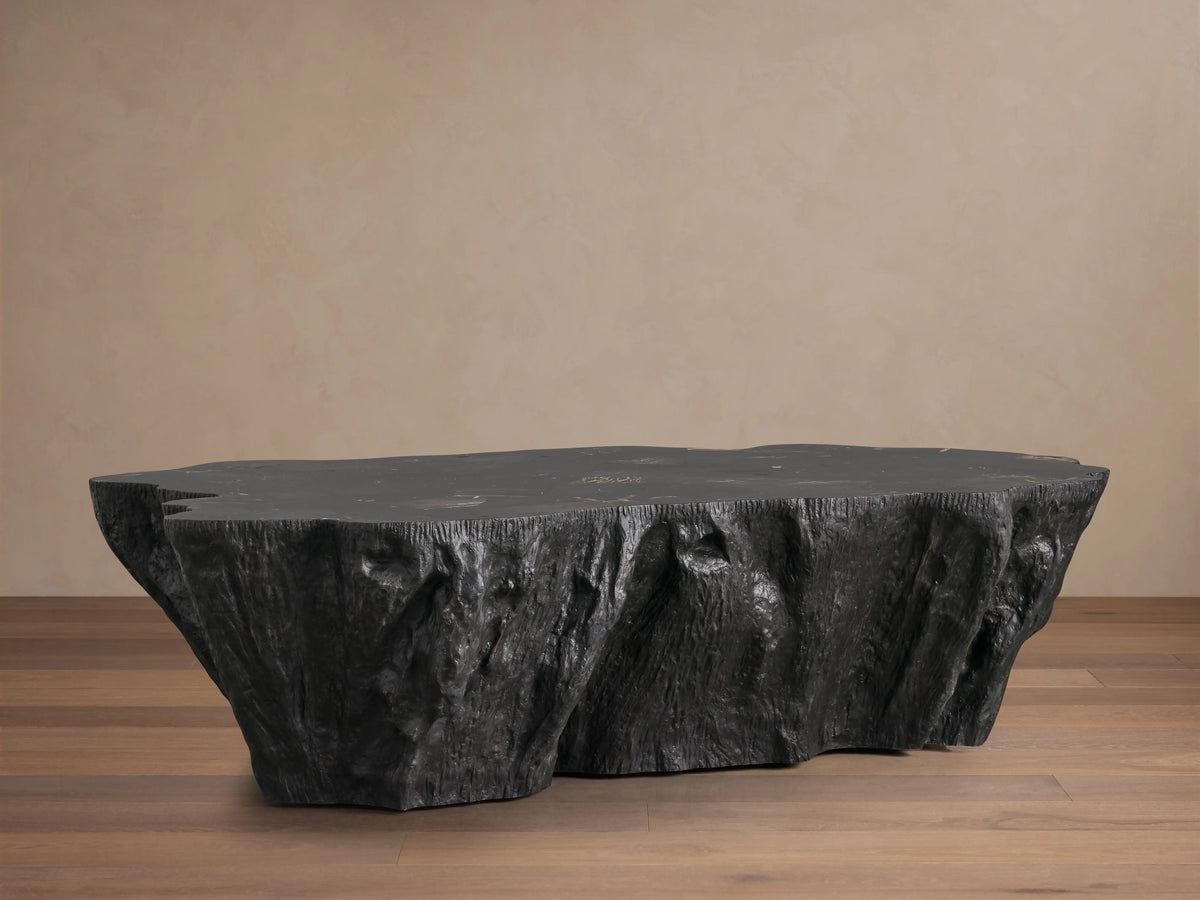 Clayhill Coffee Table made of dark petrified wood with an uneven, textured surface and organic edges, placed on hardwood floor.