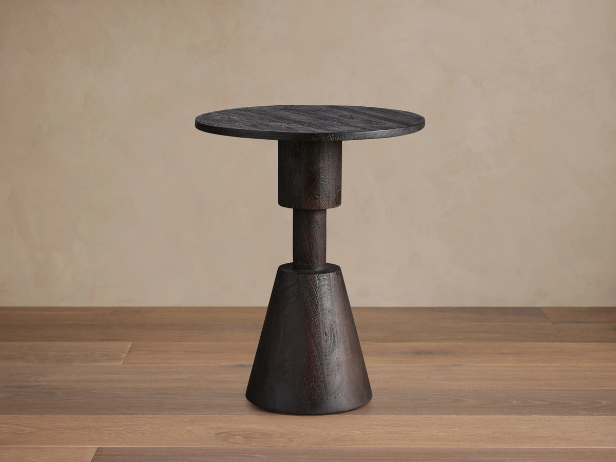 Caledonia Martini Table, dark matte brown finish. Solid mango wood. Round top, conical base. Set on wooden floor. Neutral background.