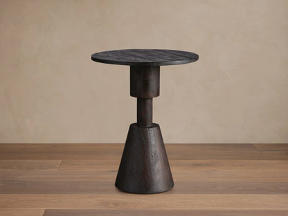 Caledonia Martini Table, dark matte brown finish. Solid mango wood. Round top, conical base. Set on wooden floor. Neutral background.