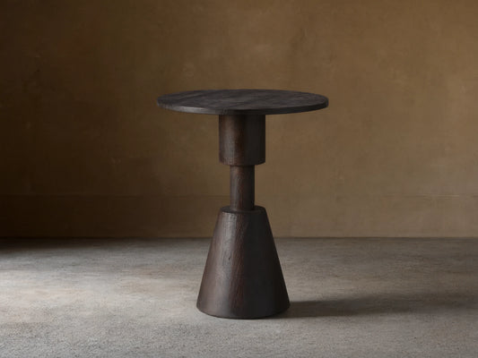 Caledonia Martini Table, dark matte brown finish. Solid mango wood. Round top, conical base. Set on wooden floor. Neutral background.