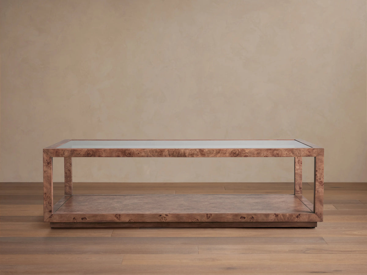 Corey Coffee Table with a rectangular shape, mappa burl wood finish, and open design. It has a top and lower surface in a light brown room setting.