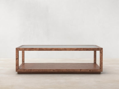 Corey Coffee Table with a rectangular shape, mappa burl wood finish, and open design. It has a top and lower surface in a light brown room setting.