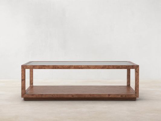 Corey Coffee Table with a rectangular shape, mappa burl wood finish, and open design. It has a top and lower surface in a light brown room setting.