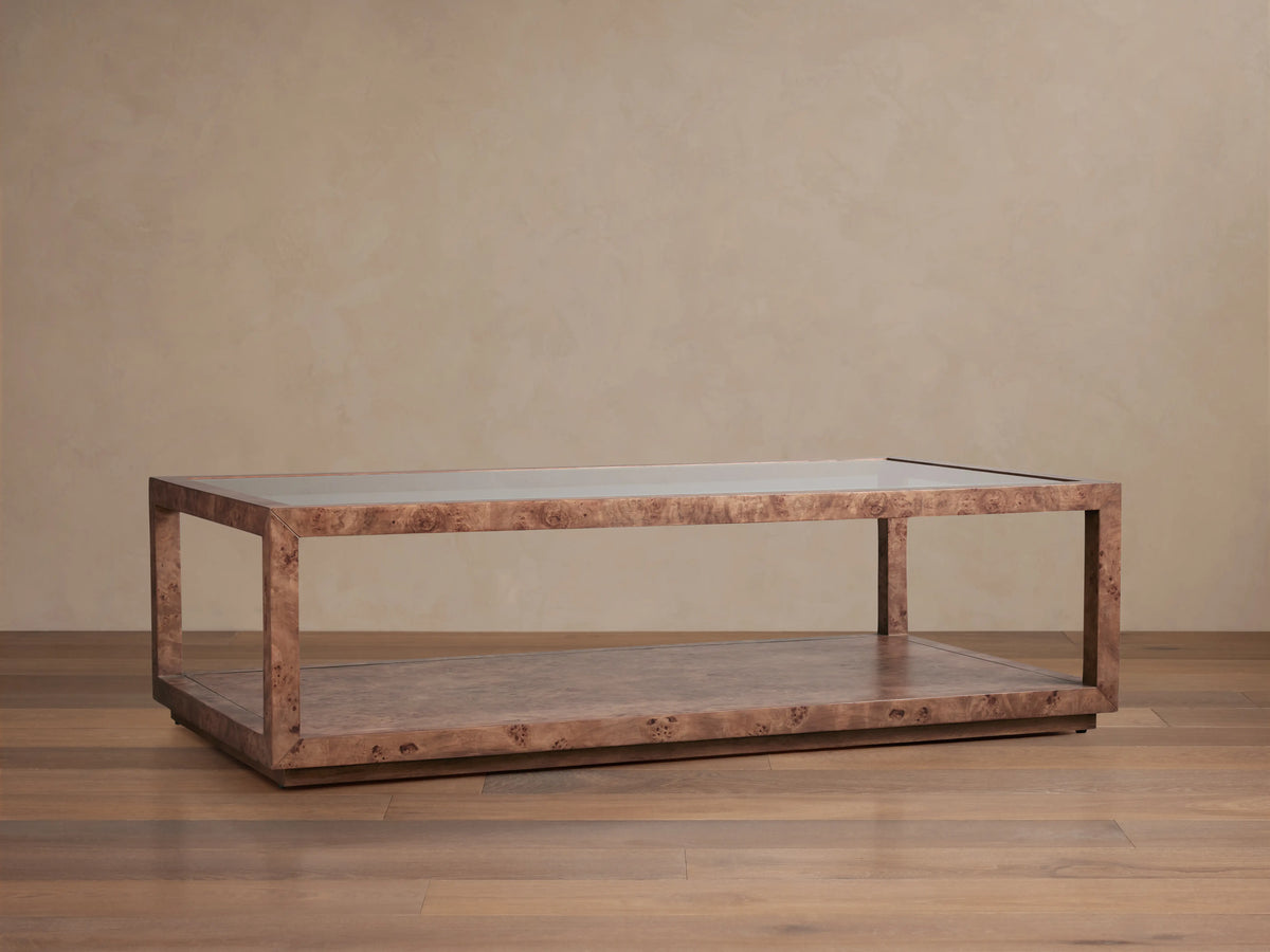 Corey Coffee Table with a rectangular shape, mappa burl wood finish, and open design. It has a top and lower surface in a light brown room setting.