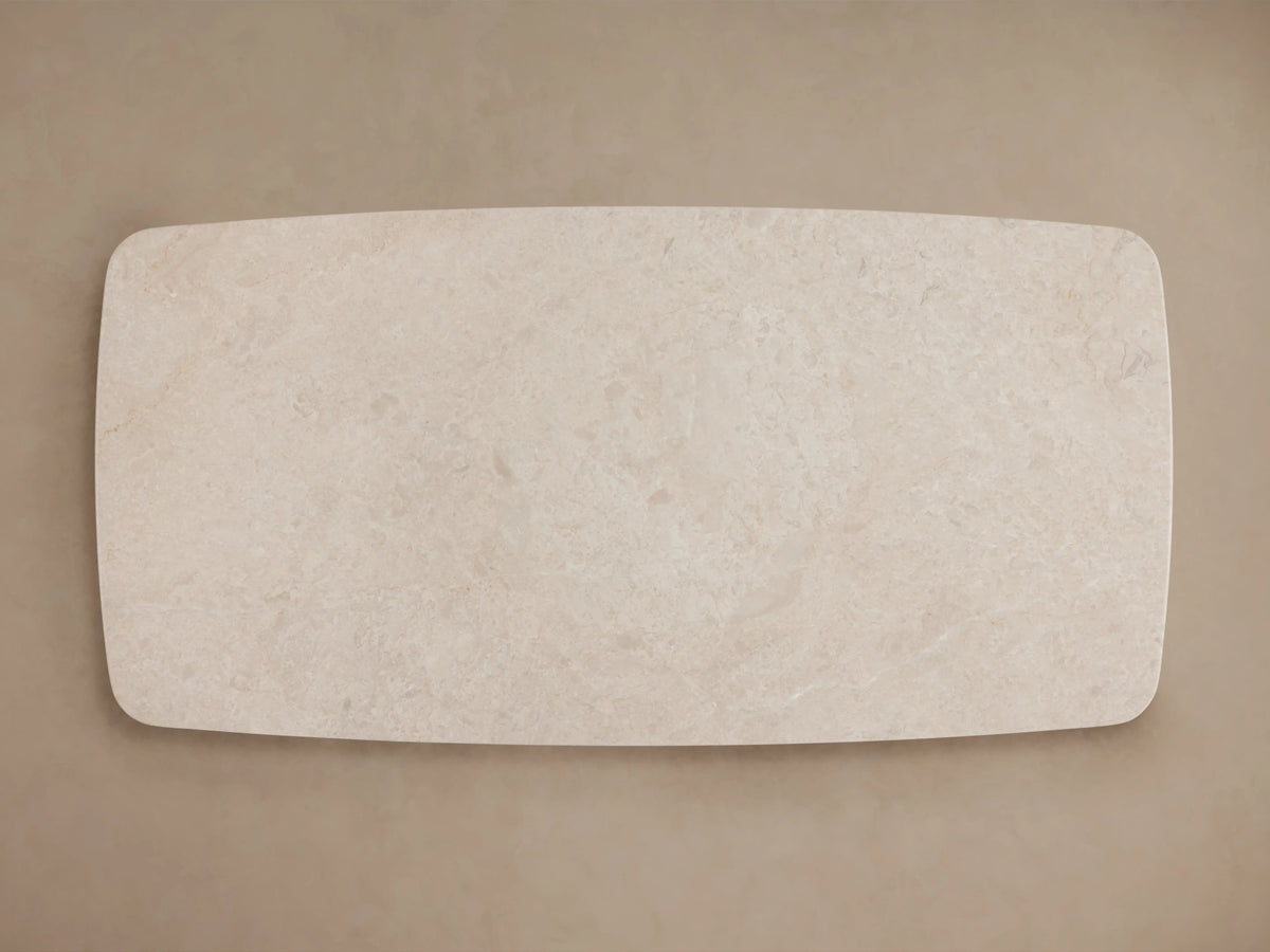 Long stone coffee table with cream marble top, set on two black cylindrical bases. Light wood floor and neutral wall backdrop.