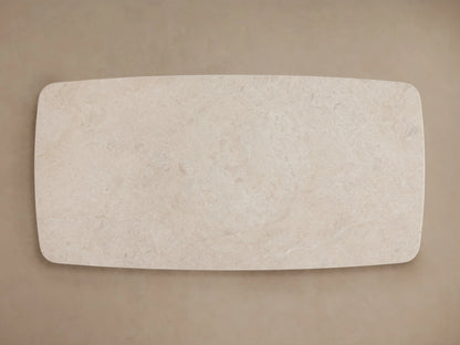 Long stone coffee table with cream marble top, set on two black cylindrical bases. Light wood floor and neutral wall backdrop.
