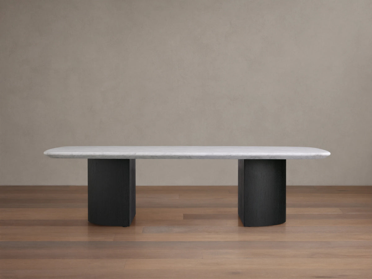 Saint Germain Stone Coffee Table with a long, oval Carrara marble top, cream color, on two solid, rectangular, dark ebony bases.