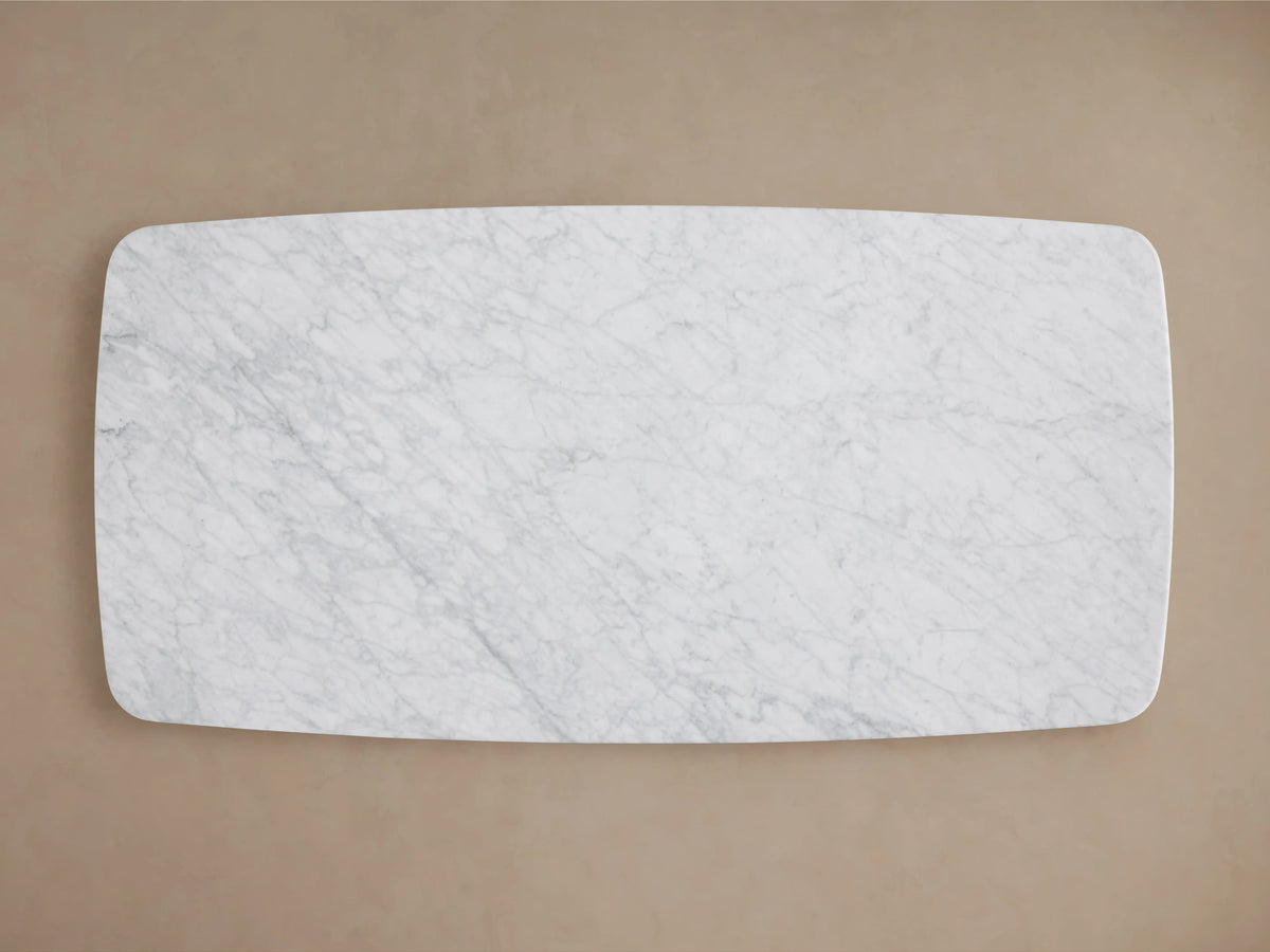 A long, rectangular coffee table with a Carrara marble top and two ebony-finished oak bases, set in a minimalistic room.