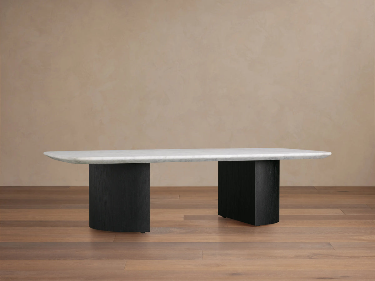 Saint Germain Stone Coffee Table with a long, oval Carrara marble top, cream color, on two solid, rectangular, dark ebony bases.