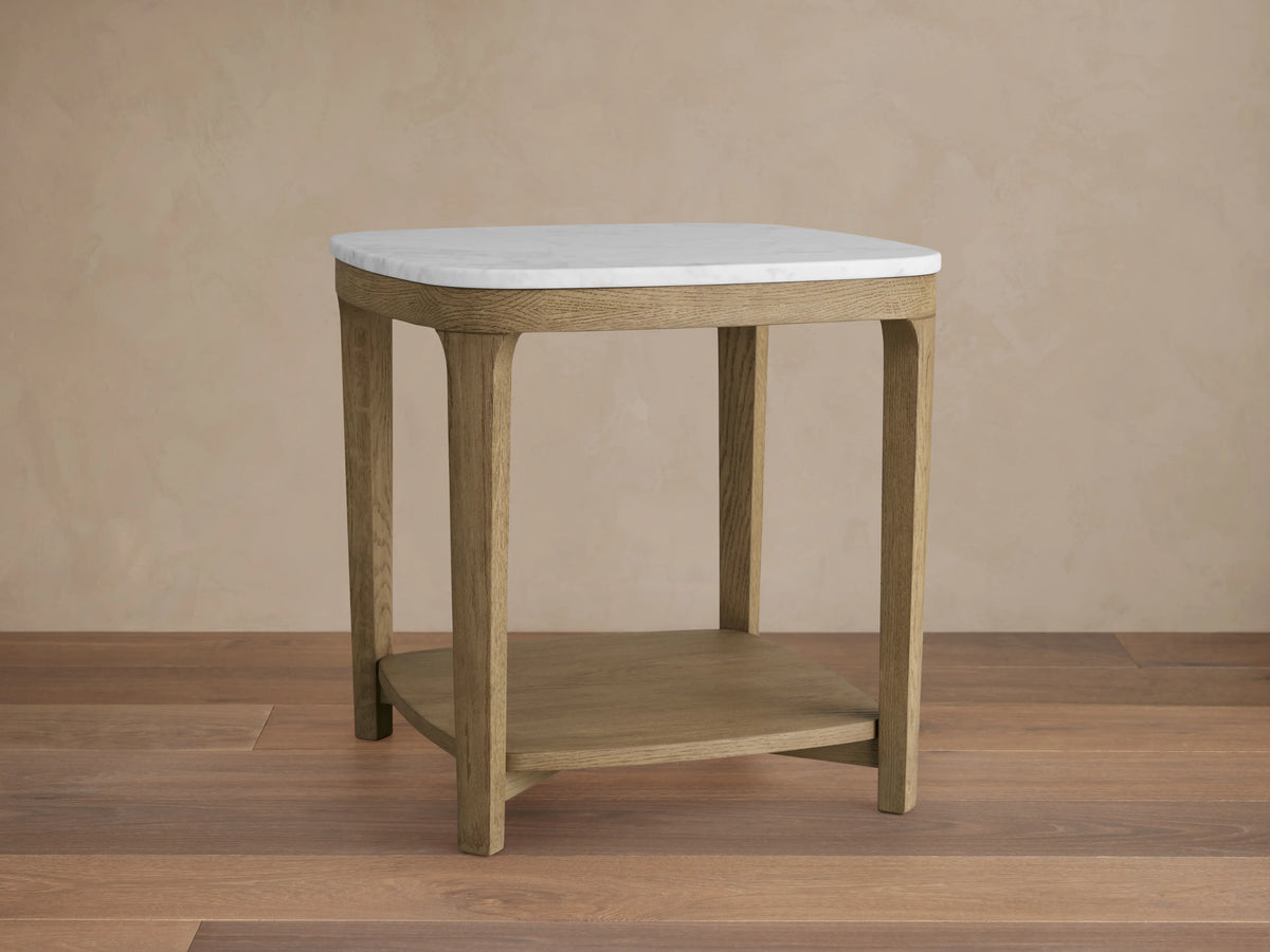 Danny End Table with an ivory-toned marble top and oak wood frame. Elegant square design with a lower shelf, set against a neutral wall.
