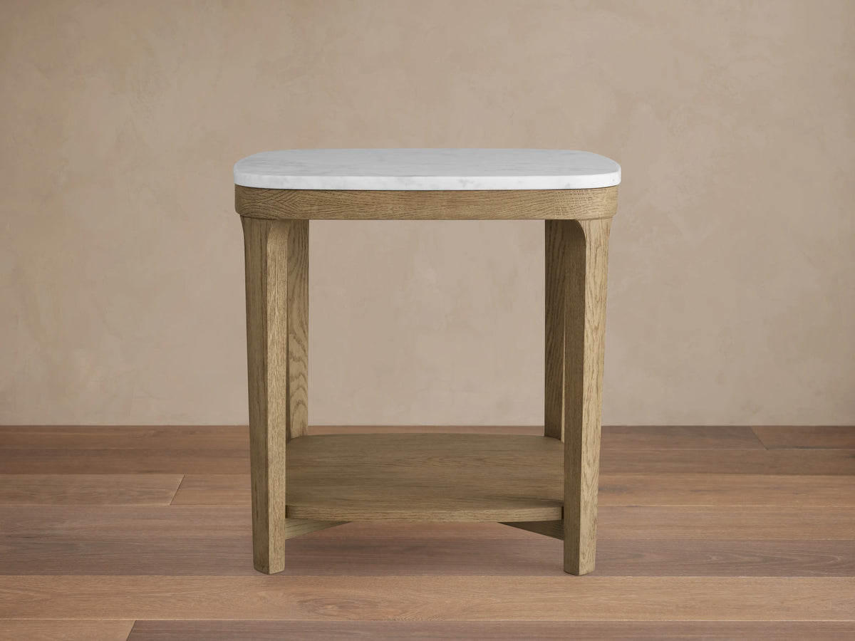 Danny End Table with an ivory-toned marble top and oak wood frame. Elegant square design with a lower shelf, set against a neutral wall.