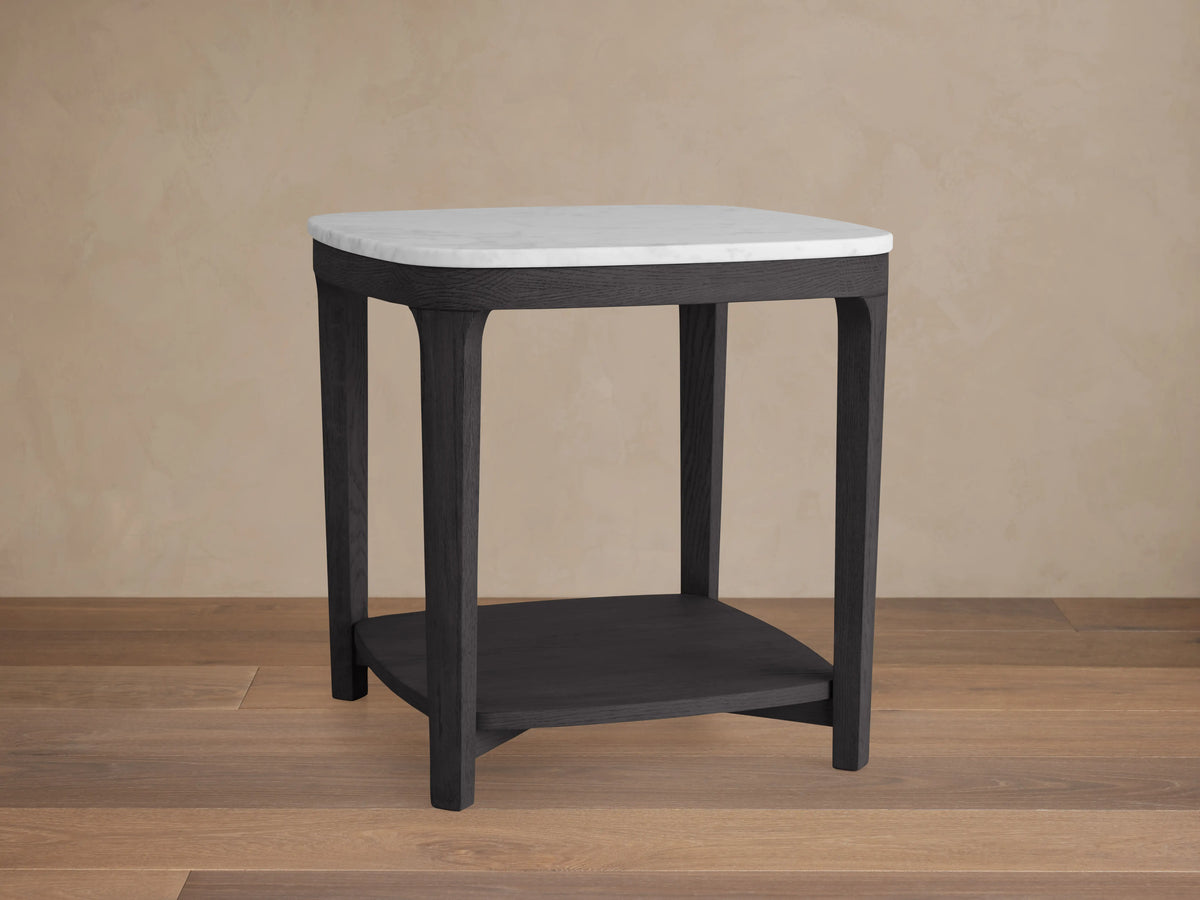 Danny End Table with ebony-finished oak wood frame and white Carrara marble top, featuring a lower shelf on a wooden floor.