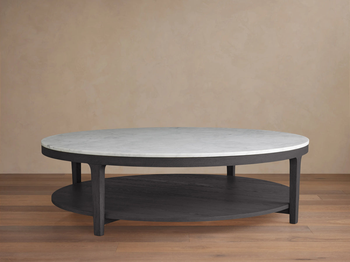 Round coffee table with ebony-finished oak frame and white marble top. Features a lower shelf, placed on wooden flooring.