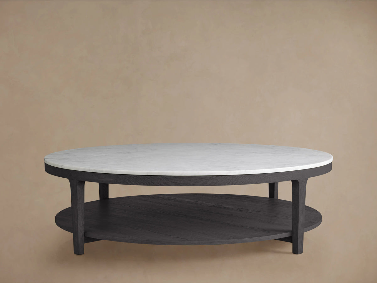 Round coffee table with an ebony-finished oak wood base and a white Carrara marble top, set against a beige background.