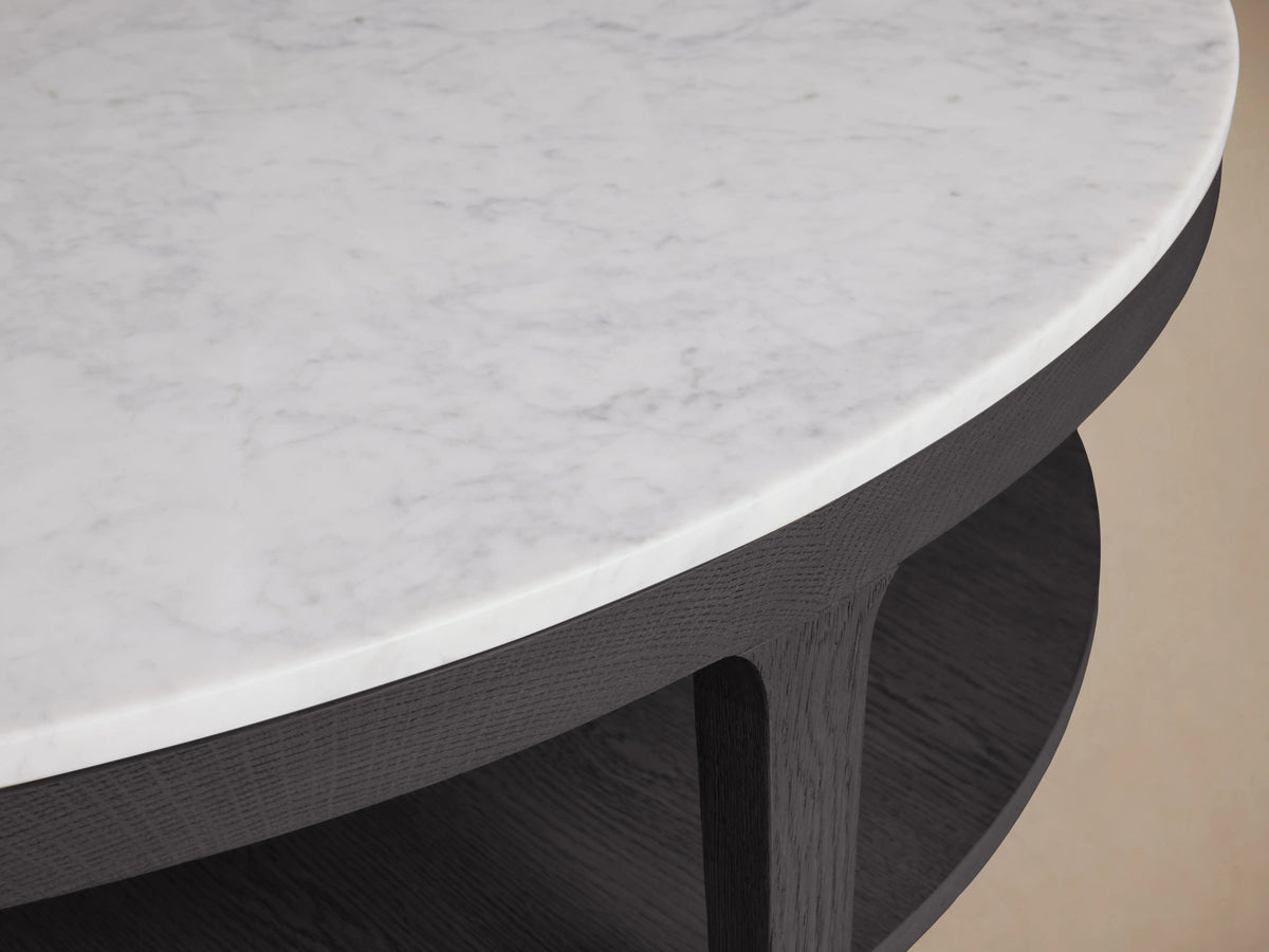 Danny Round Coffee Table with a white Carrara marble top, dark oak wood base, and lower shelf, set on wooden flooring.