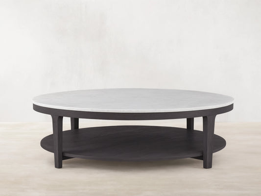 Danny Round Coffee Table with a white Carrara marble top and ebony oak base, featuring a two-tier design on a wooden floor background.