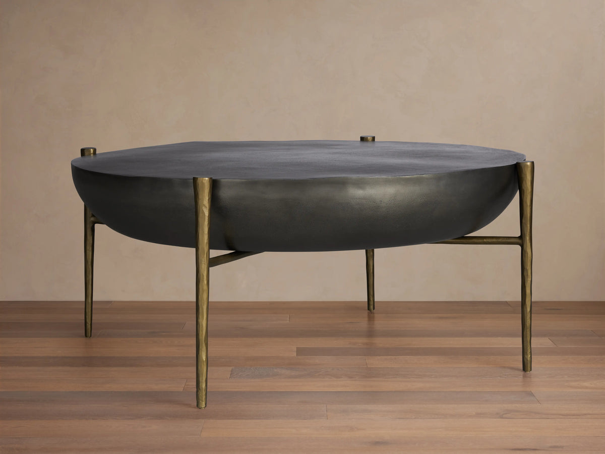 Donovan Coffee Table with a textured black nickel surface and antique brass legs on a wooden floor.