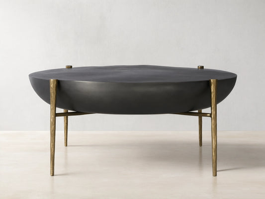 Donovan Coffee Table in black nickel finish with round, textured cast aluminum top, antique brass legs, on wooden floor.