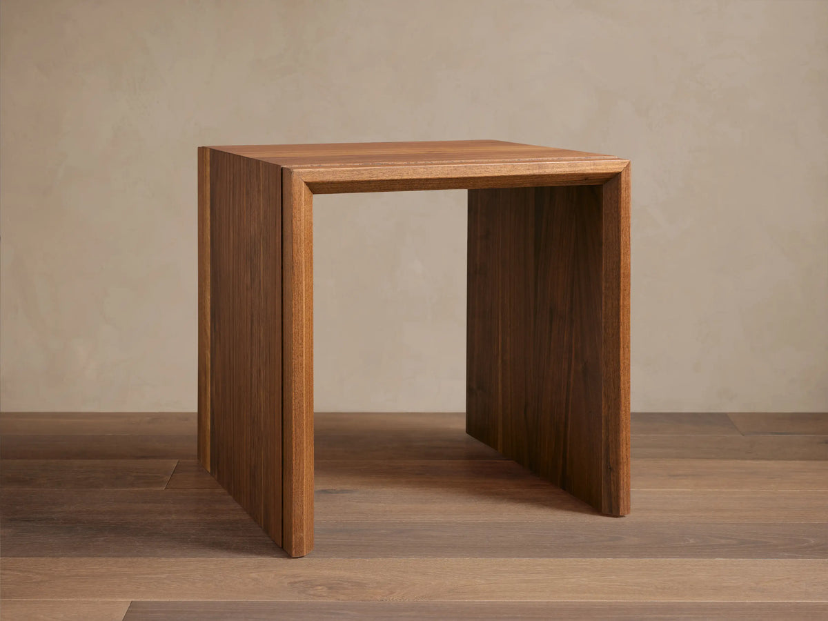 Elien Nesting End Table with a square, minimalist design made of rich wood, positioned on a wooden floor against a plain wall.