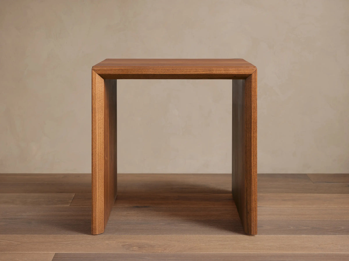 Elien Nesting End Table with a square, minimalist design made of rich wood, positioned on a wooden floor against a plain wall.