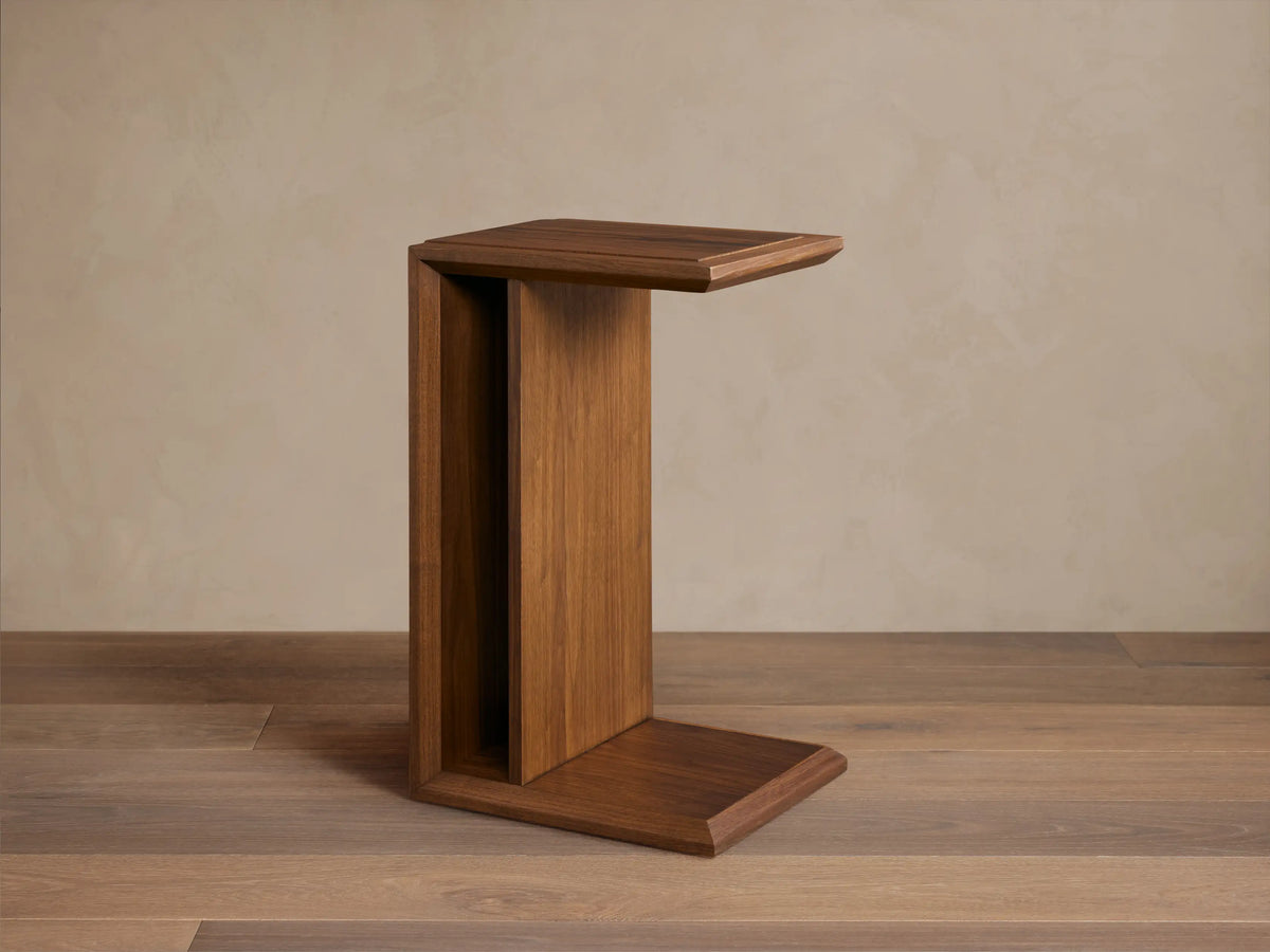 Elien C Table in a rich brown wood finish on a wooden floor, featuring a minimalist C-shape design.