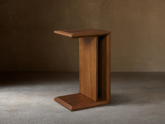 Elien C Table in a rich brown wood finish on a wooden floor, featuring a minimalist C-shape design.