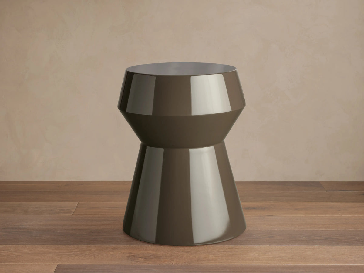 Eris Lacquer Stool in a brown high-gloss finish. Hourglass shape with a wide top and base, placed on a wooden floor.