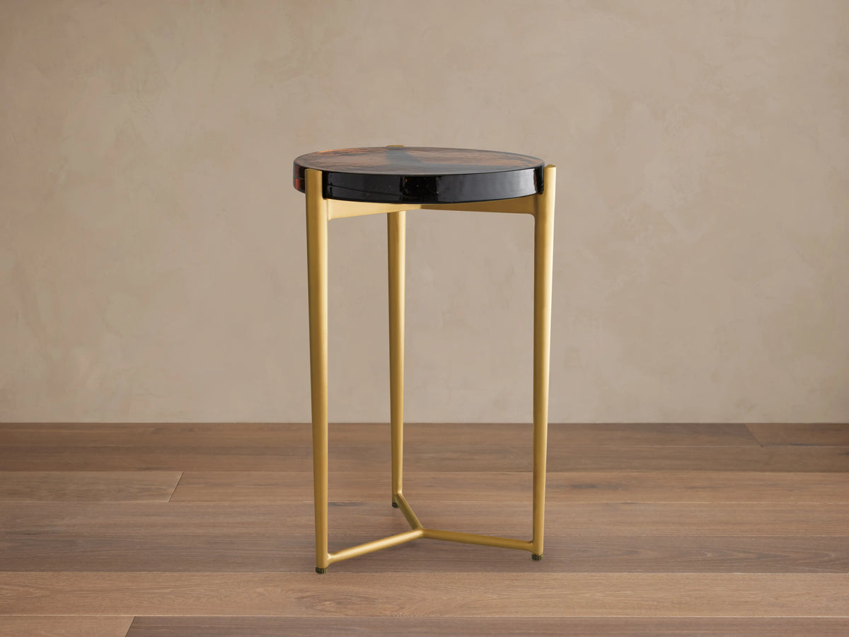 Ezio Martini Table with a round black glass top featuring unique bubbles. Three-legged gold iron base on a wooden floor.