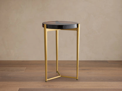 Ezio Martini Table with a round black glass top featuring unique bubbles. Three-legged gold iron base on a wooden floor.