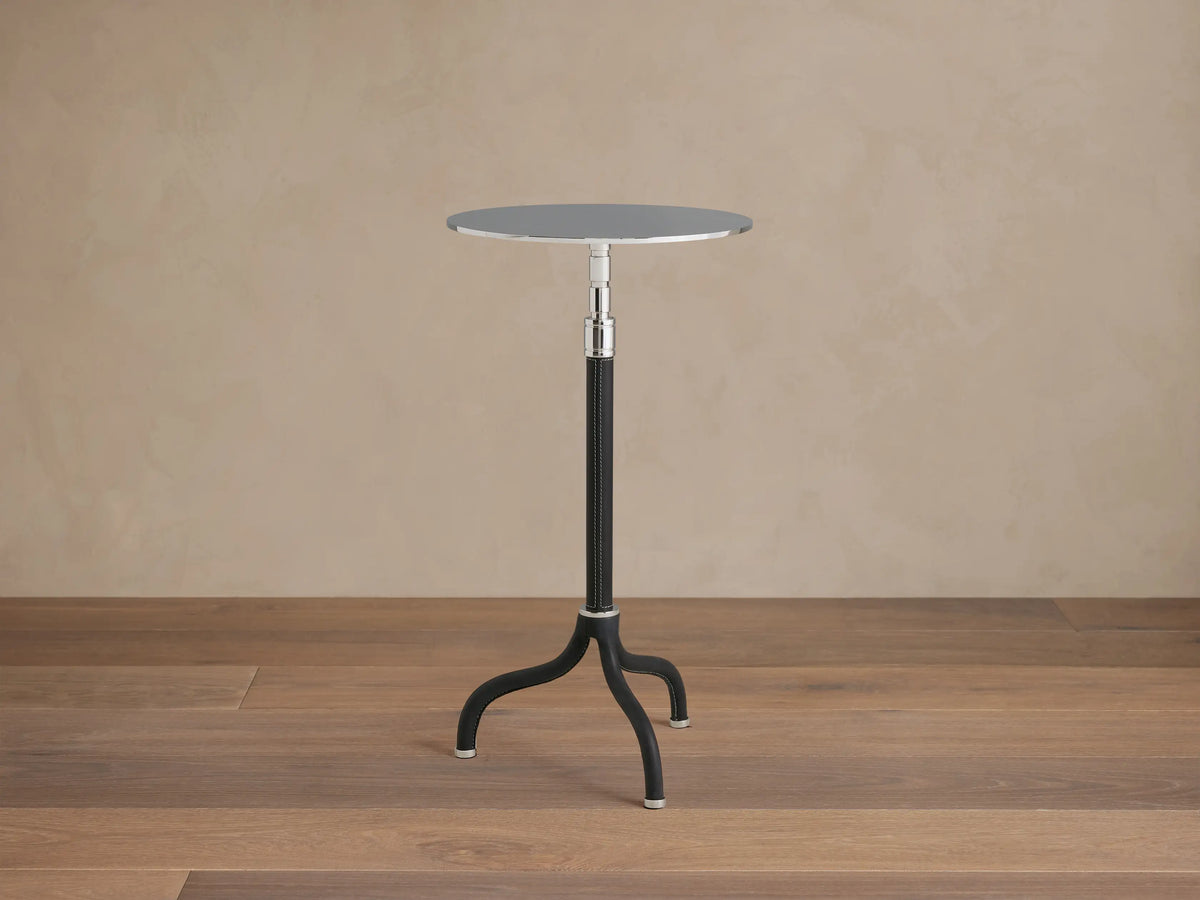Ferdinand Leather Martini Table on a wooden floor, featuring a slender black tripod base and round brass-finished tabletop.