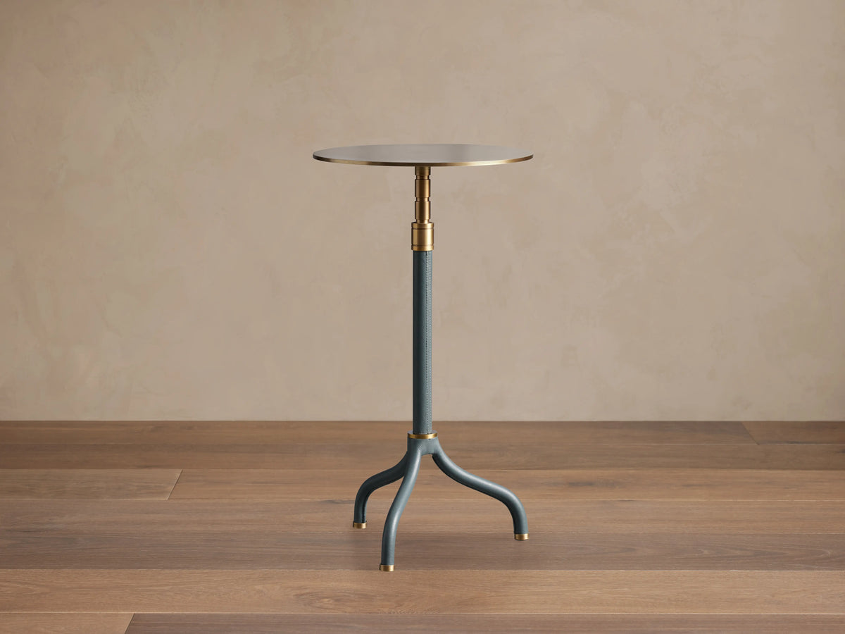 Ferdinand Leather Martini Table with blue leather-wrapped stem, brass accents, and a brass-finished tabletop on a wooden floor.