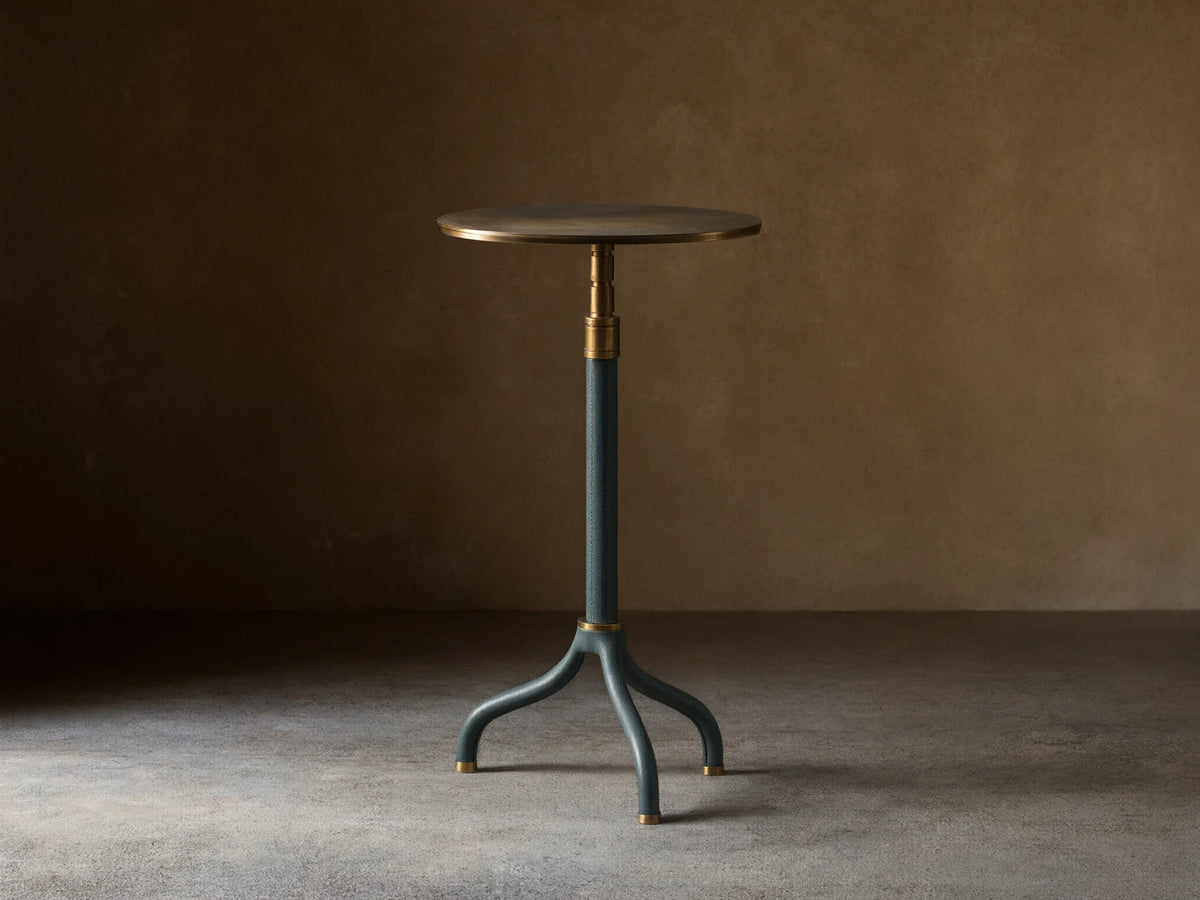 Ferdinand Leather Martini Table with blue leather-wrapped stem, brass accents, and a brass-finished tabletop on a wooden floor.