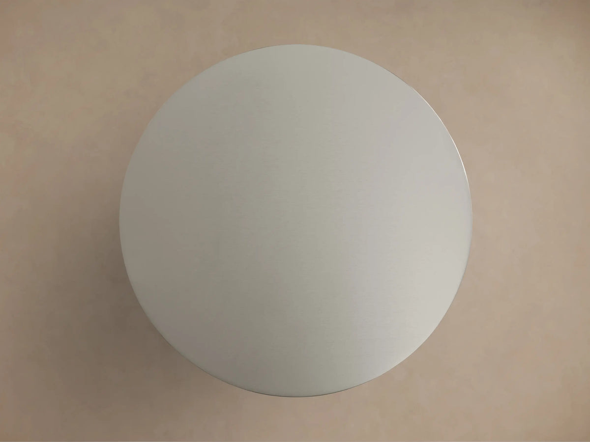 Ferdinand Martini Table with a sleek, round metallic top and sturdy cylindrical base shown against a beige background.