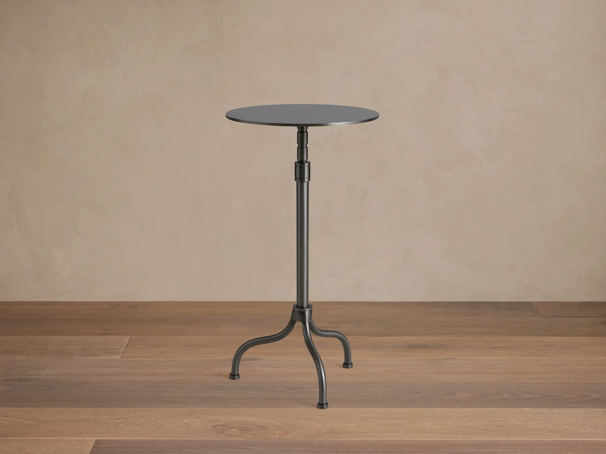 Ferdinand Martini Table with a sleek black round top, supported by a slender metal pedestal and three curved legs on wood floor.