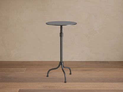 Ferdinand Martini Table with a sleek black round top, supported by a slender metal pedestal and three curved legs on wood floor.