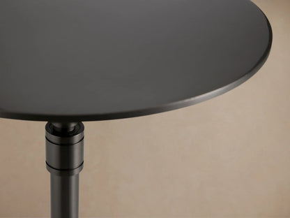 Ferdinand Martini Table with a sleek black round top, supported by a slender metal pedestal and three curved legs on wood floor.