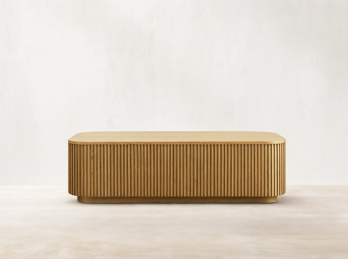 Finnley Wood Coffee Table in Honey finish, rectangular with rounded edges, features vertical slatted design on sides, on wood floor.