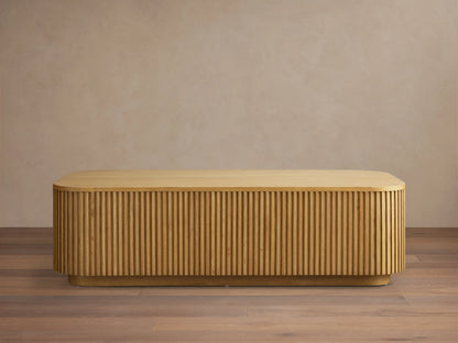 Finnley Wood Coffee Table in Honey finish, rectangular with rounded edges, features vertical slatted design on sides, on wood floor.