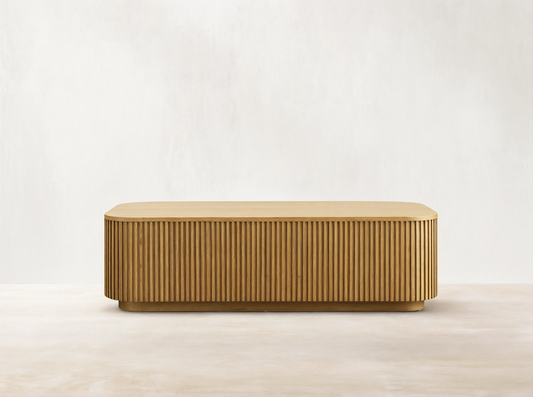 Finnley Wood Coffee Table in Honey finish, rectangular with rounded edges, features vertical slatted design on sides, on wood floor.