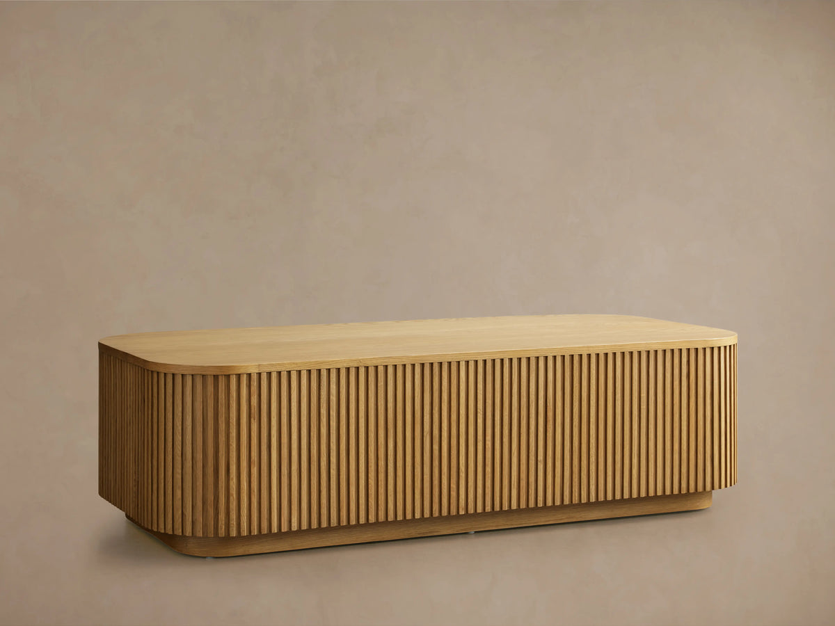 Finnley Wood Coffee Table in Honey finish, rectangular with rounded edges, features vertical slatted design on sides, on wood floor.
