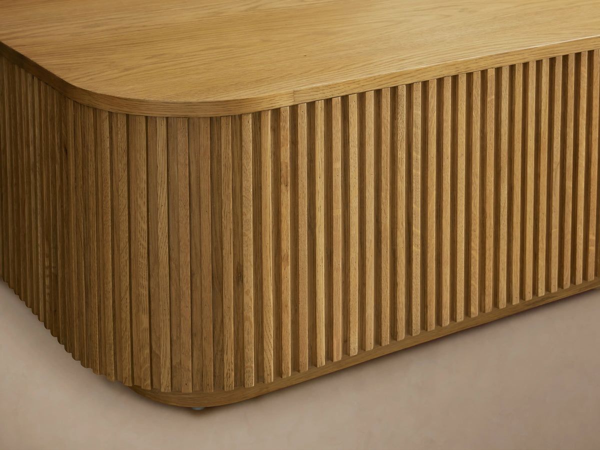 Finnley Wood Coffee Table in honey finish; rectangular with rounded edges. Features vertical slat design on sides, smooth top.