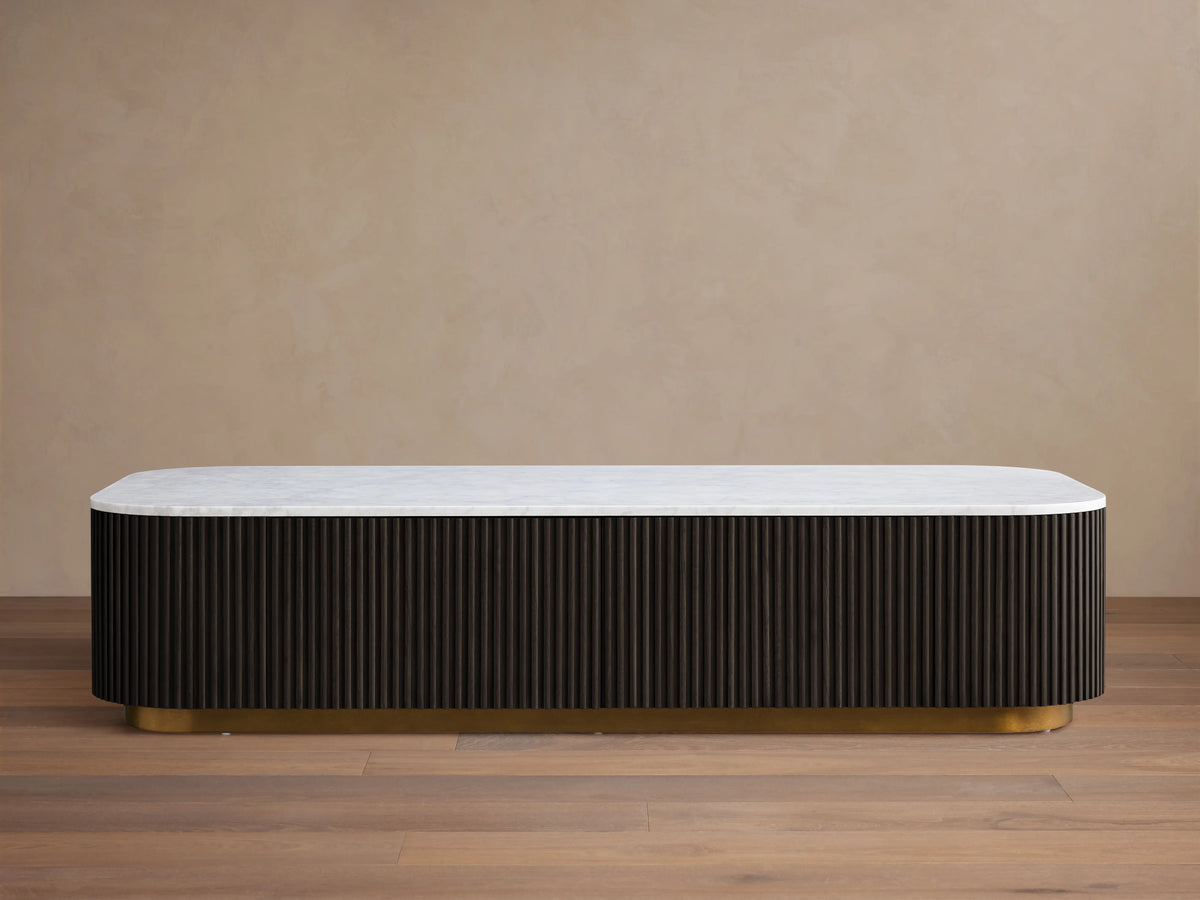 Finnley Storage Coffee Table with a white top and dark ribbed sides on a brass-finished base, on a wooden floor.