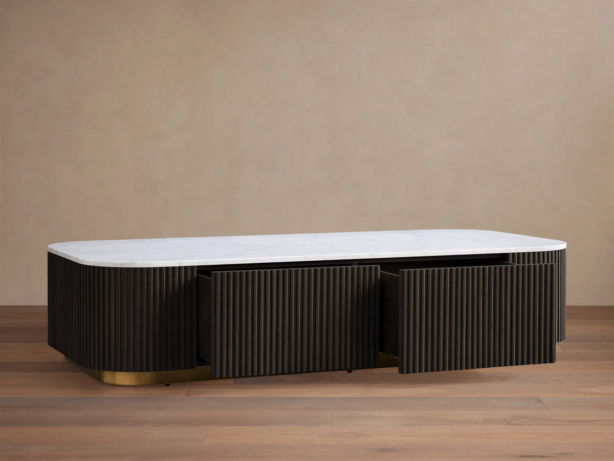 Finnley Storage Coffee Table with a white top and dark ribbed sides on a brass-finished base, on a wooden floor.