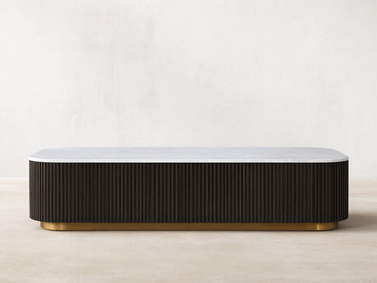 Finnley Storage Coffee Table with a white top and dark ribbed sides on a brass-finished base, on a wooden floor.