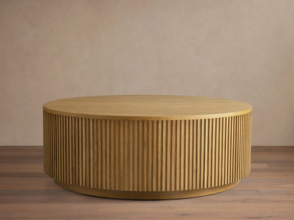 Finnley Round Wood Coffee Table in Honey finish, featuring a circular shape with vertical slats, placed on wooden flooring.